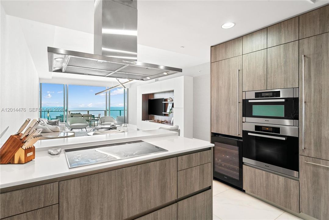 Kitchen with Living Room View – Designed for both style and function, the kitchen includes built-in ovens, full-height cabinetry, a wine cooler, and a generous prep surface. The open sightline to the living room and water view adds to the home’s airy feel.