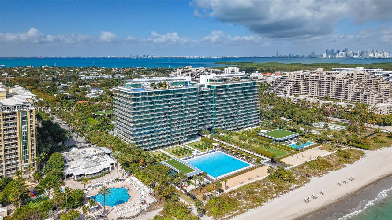 Aerial Oceanfront Community View – A wide aerial perspective highlights the building, beach, pool areas, and surrounding coastal community. The view captures both the oceanfront setting and the broader island landscape.