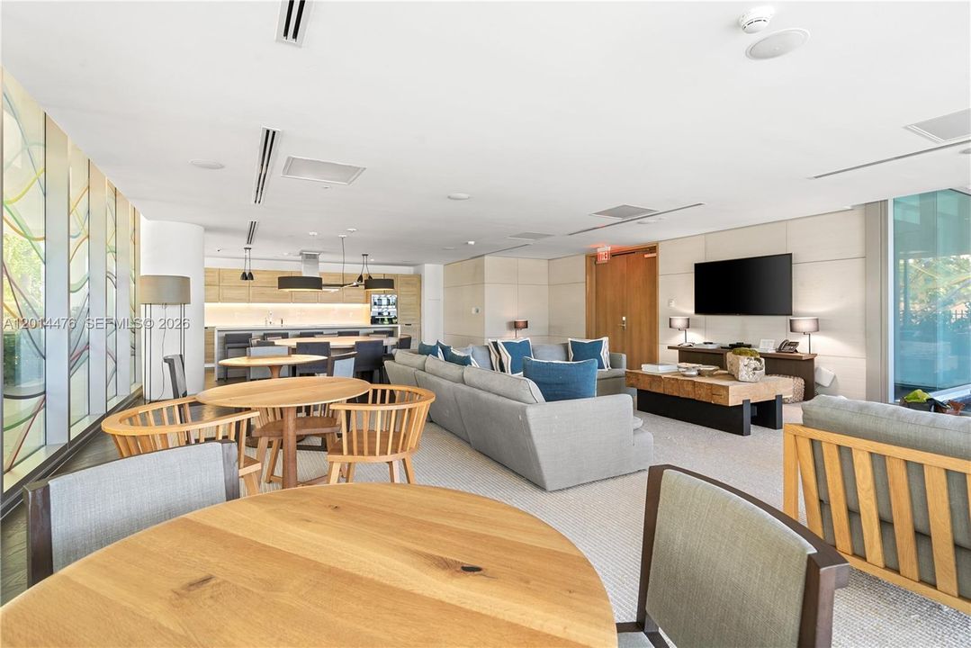 Amenity Lounge / Dining Area – This amenity space offers multiple seating areas, dining tables, and an open kitchen for flexible entertaining. Floor-to-ceiling glass and warm wood details add light and texture throughout the room.
