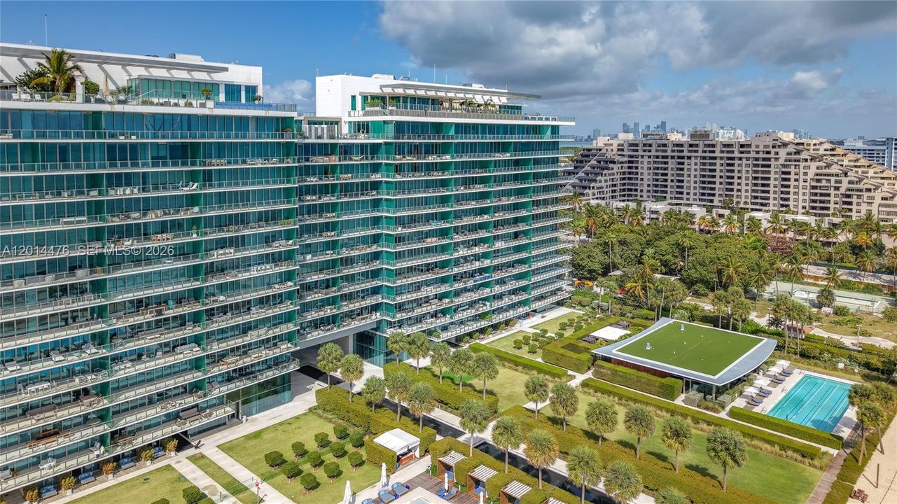 Building Exterior – The modern glass-fronted building is shown with manicured grounds, palm-lined landscaping, and resort-style amenities below. Its expansive balconies and sleek architecture create a striking waterfront presence.