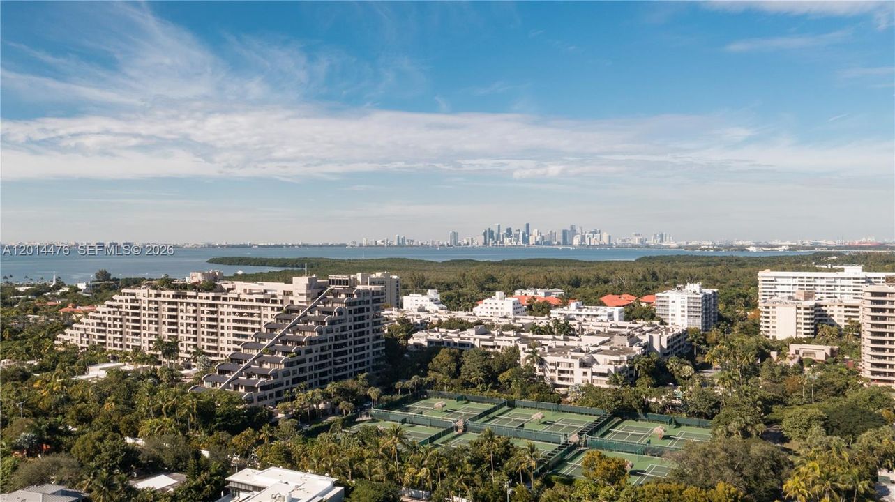 Skyline and Bay View – This elevated view looks across the island toward Biscayne Bay and the distant city skyline. Tennis courts, tropical landscaping, and surrounding residences add depth to the expansive outlook.