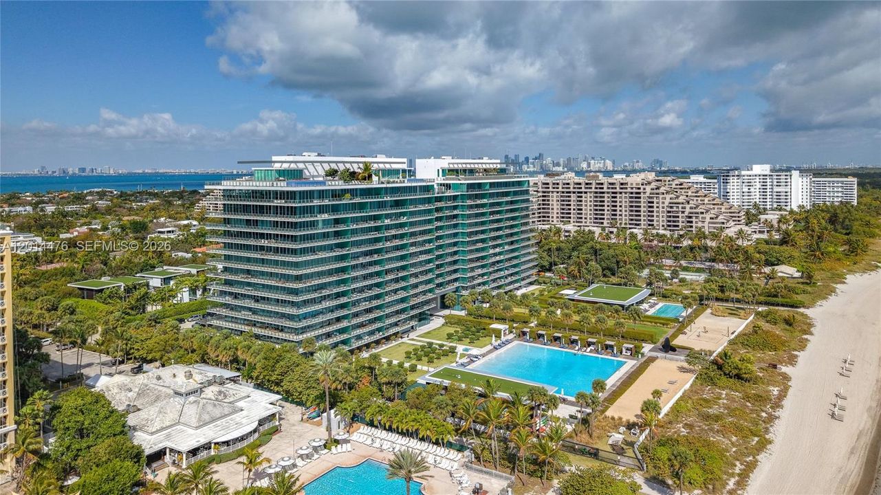 Aerial Exterior with Skyline Views – This elevated angle captures the building, surrounding residences, Biscayne Bay, and the distant skyline. The property is positioned within a lush coastal setting with water views in multiple directions.