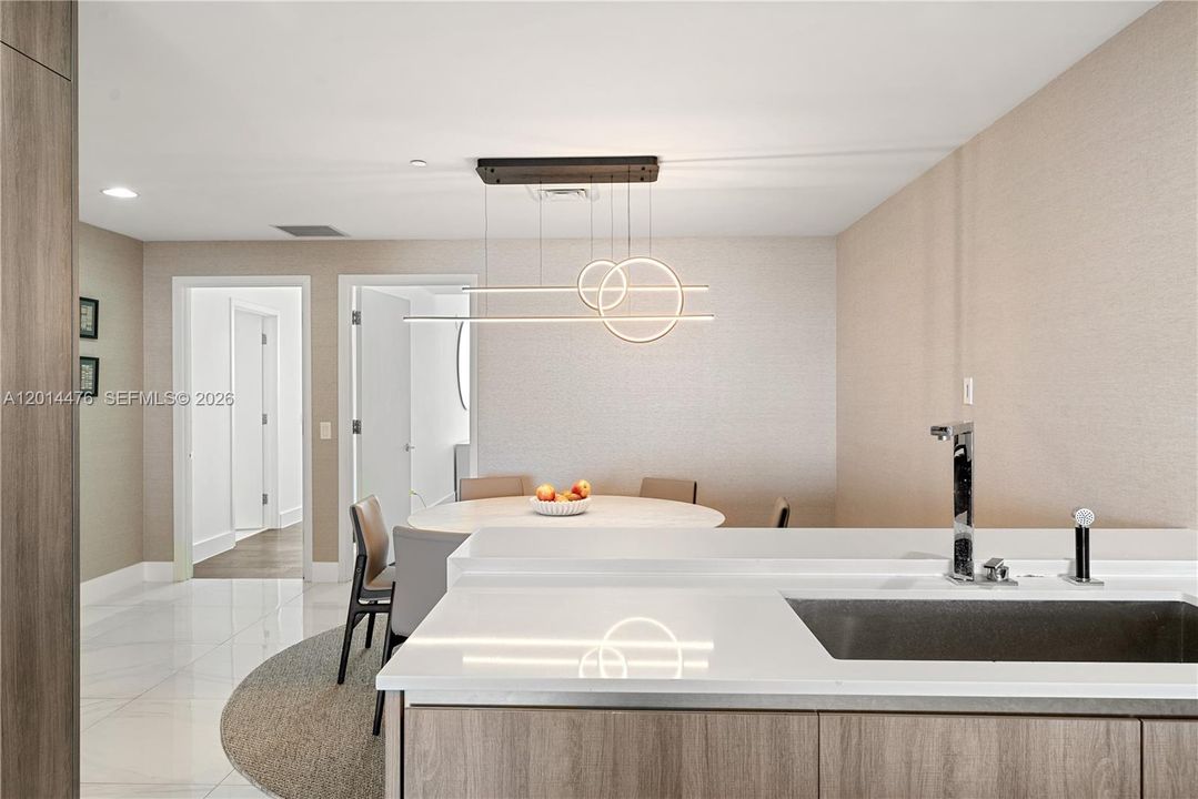 Dining Area – The dining area sits just off the kitchen and is accented by a sculptural modern chandelier. Neutral wallcovering, glossy flooring, and a rounded dining table create a polished setting for meals or casual gatherings.
