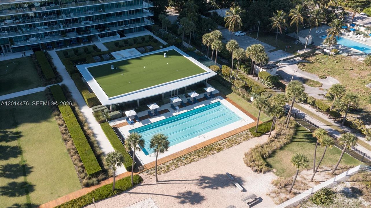Aerial Amenity View – This elevated angle showcases the lap pool, landscaped lawns, beach pathway, and amenity areas adjacent to the building. The layout offers a clear look at the property’s outdoor spaces and direct access toward the shoreline.