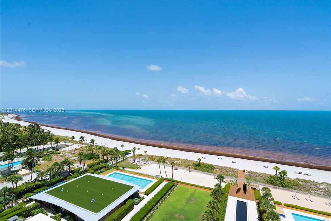 Oceanfront View – A sweeping elevated view captures the beach, turquoise water, and beautifully landscaped outdoor amenities below. The wide horizon and vibrant coastal setting create a striking visual connection to the ocean.