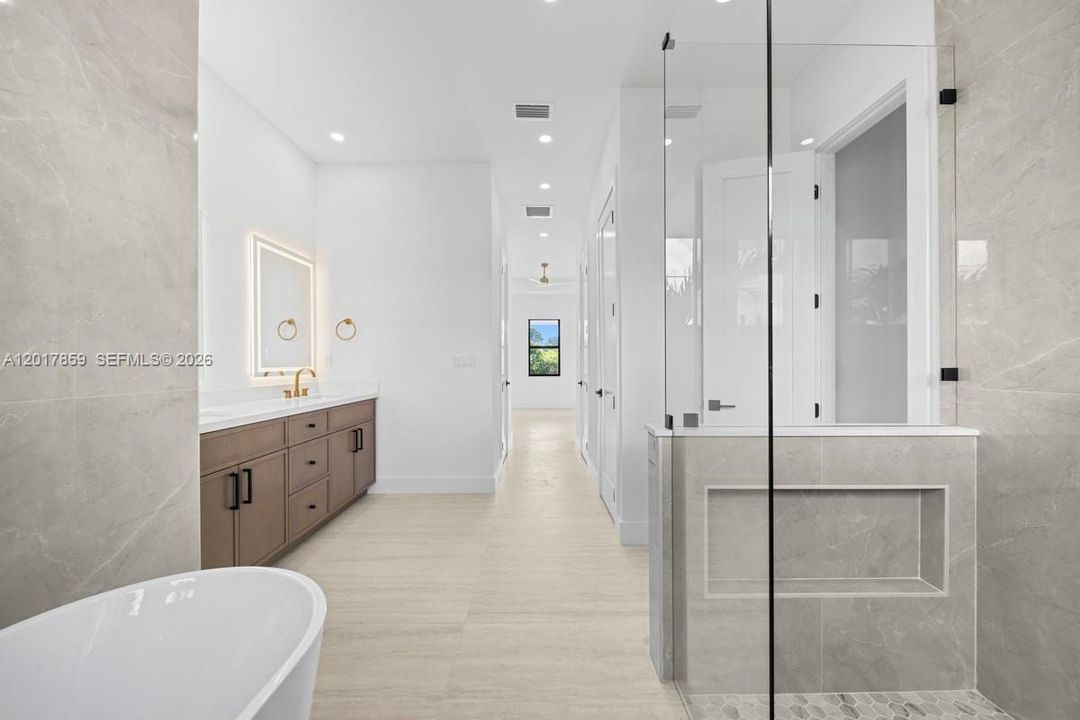 Bathroom featuring a large-format tile shower with a glass enclosure, a freestanding soaking tub, a wood-finish vanity with hardware, and an LED-backlit mirror