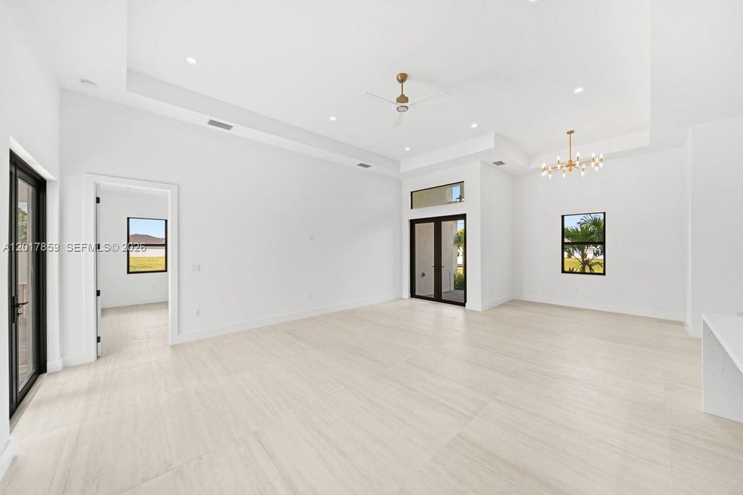 Open interior space featuring tray ceilings, wood-finish tile flooring, recessed lighting, a multi-arm chandelier, and glass-paned double doors