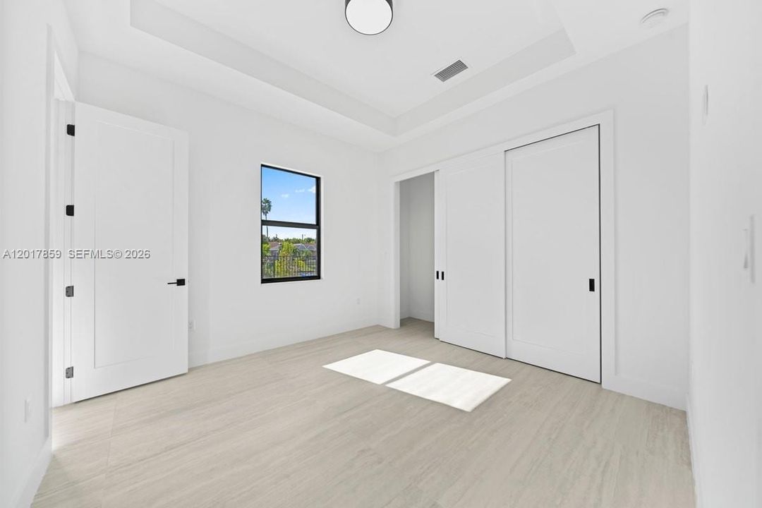 Tray ceiling with integrated lighting, wood-finish flooring, sliding closet doors, and black window and door hardware