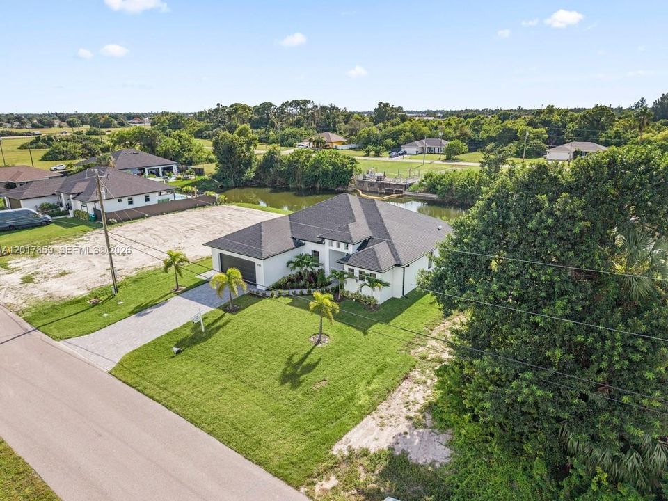 Single-story residence featuring a multi-gable roofline, paved driveway, expansive lawn, mature palm trees, and waterfront lot positioning