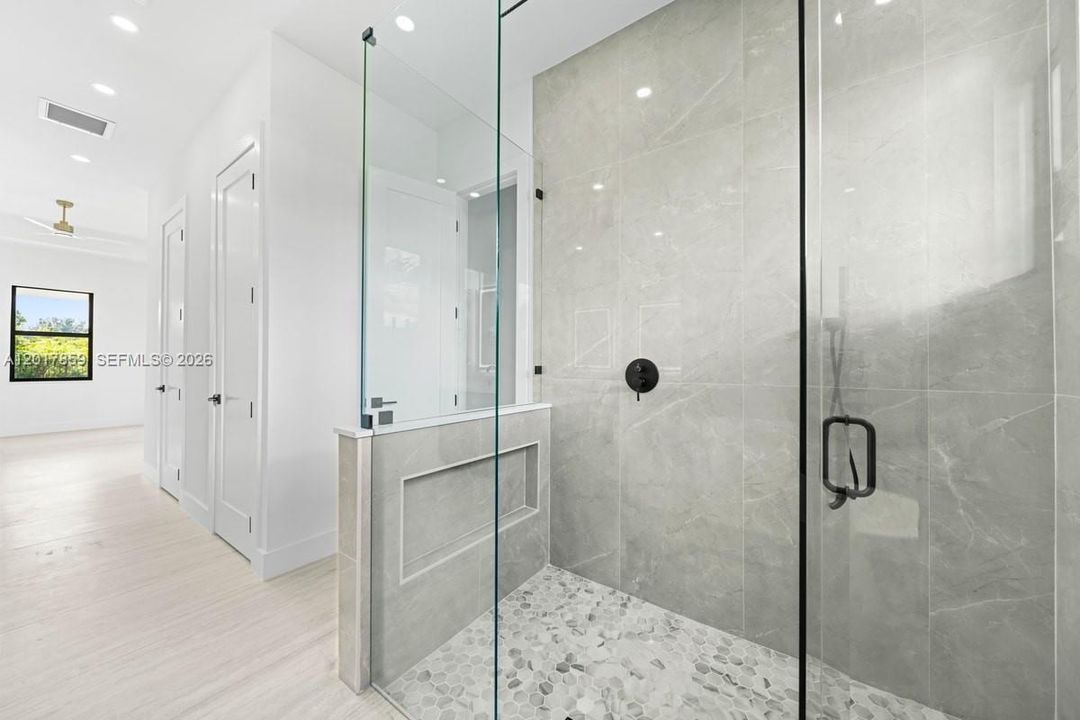 Walk-in shower featuring large-format stone-finish tile surround, pebble tile flooring, built-in recessed wall niche, frameless glass enclosure, and matte black hardware