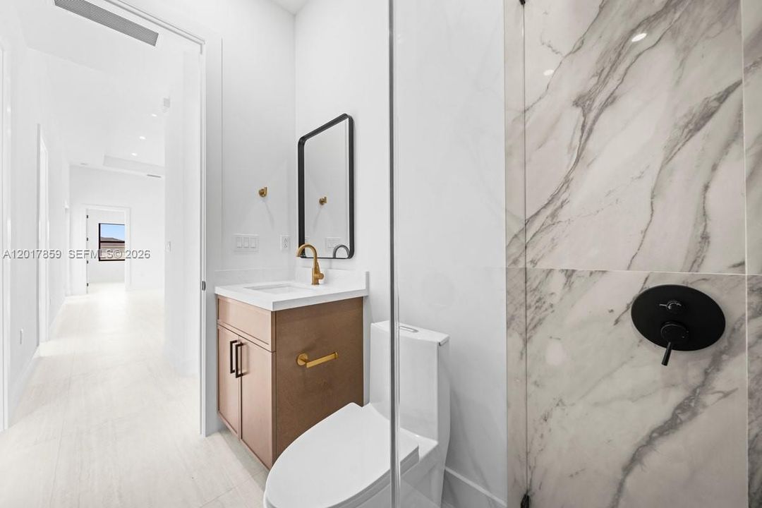 Bathroom featuring a vanity with a white countertop and gold-toned faucet, large-format stone-patterned shower tiling, frameless glass shower enclosure, matte black shower fixtures, and rectangular wall-mounted mirror with a black frame