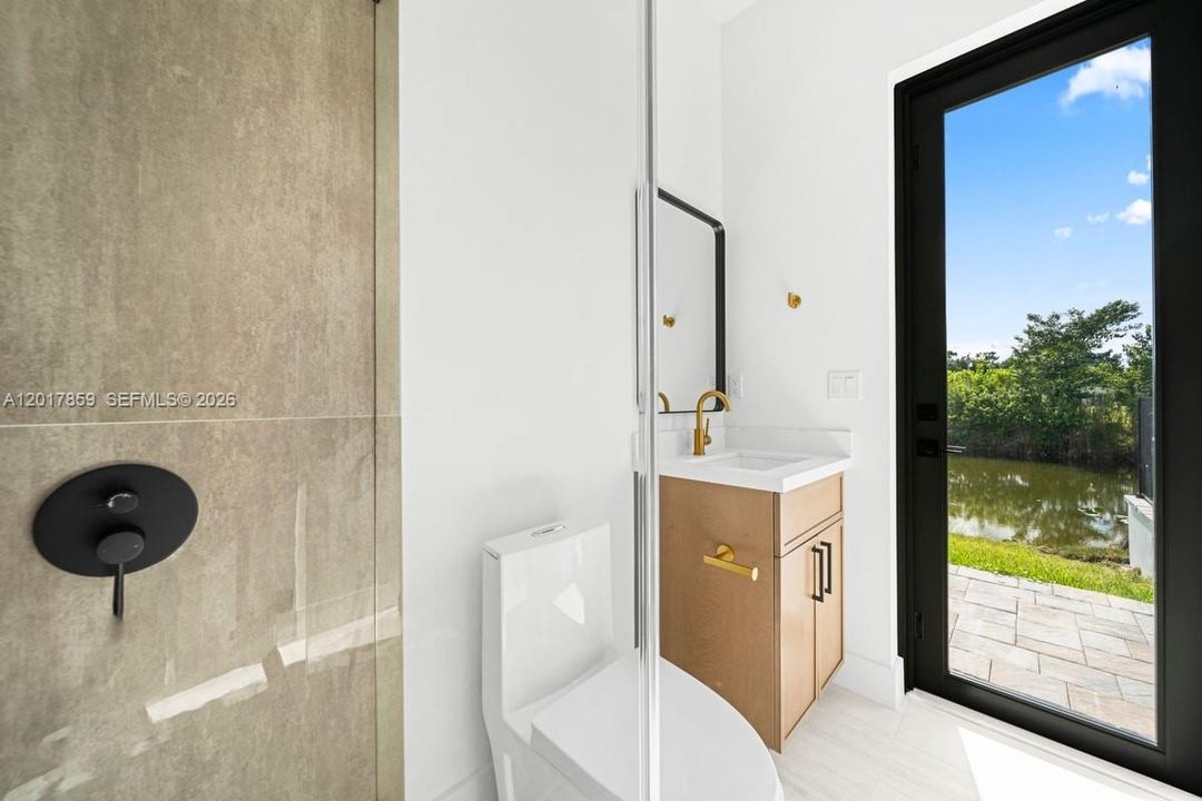 Walk-in shower featuring oversized stone-finish wall tile and matte black fixtures, wood-finish vanity with white countertop, and glass exterior door opening to a paved patio