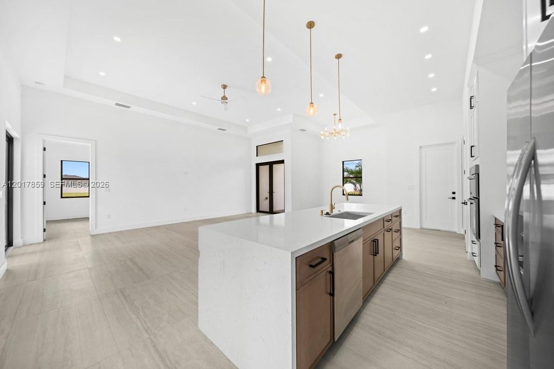 Kitchen featuring a large central island with quartz countertops, wood-finish cabinetry, recessed ceiling lighting, pendant light fixtures, and tile flooring