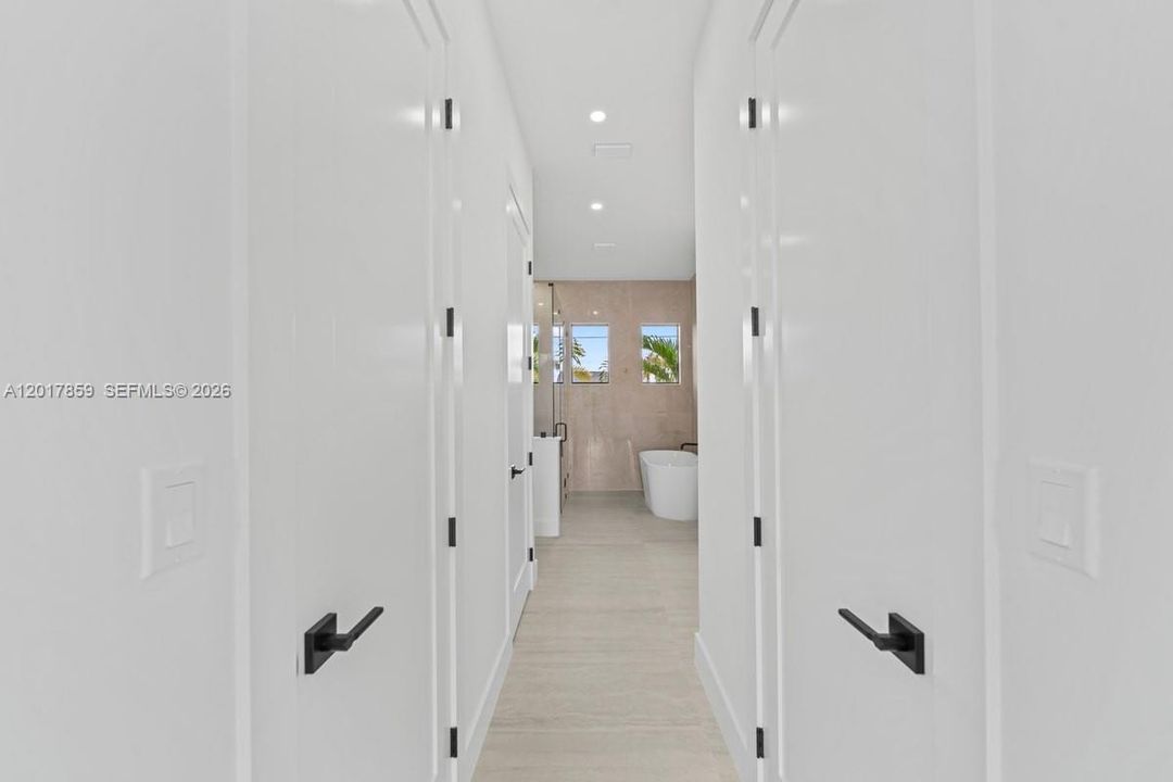 Hallway featuring white panel doors with matte black hardware, recessed ceiling lighting, and light-toned tile flooring