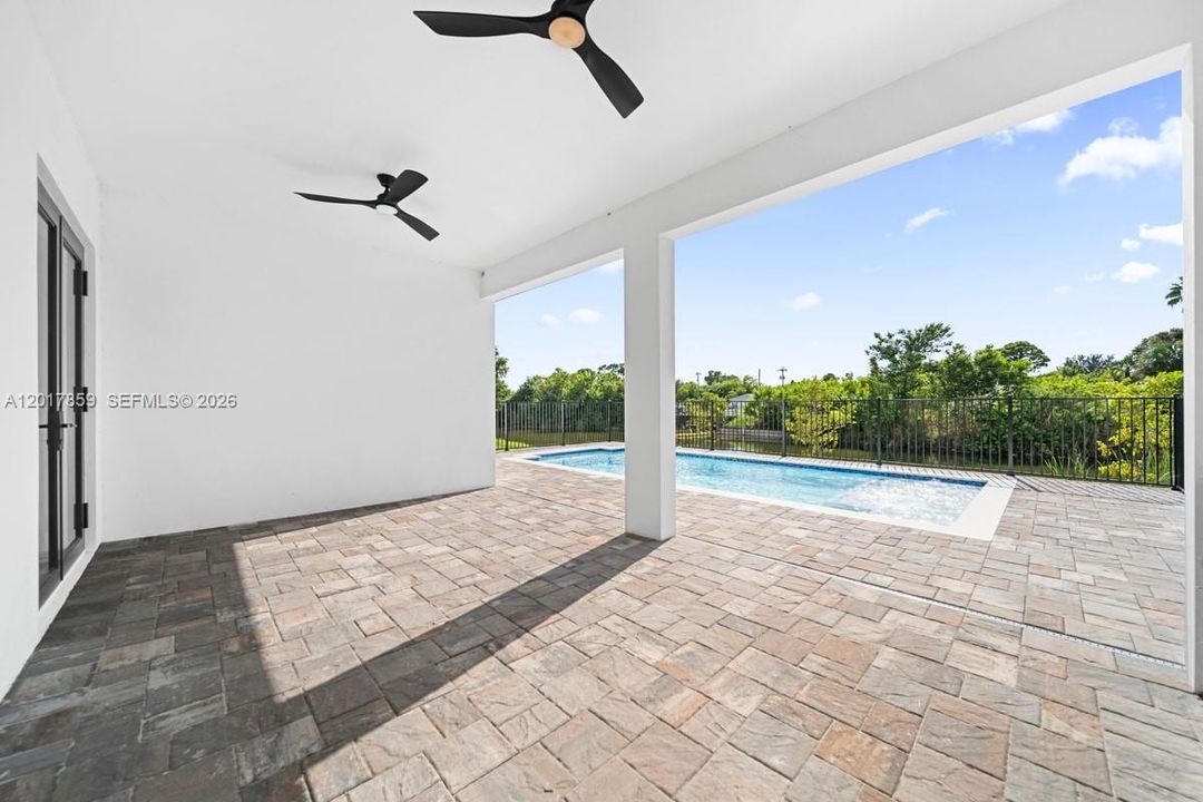 Covered patio featuring paver flooring, dual matte black ceiling fans, and an in-ground pool with a perimeter fence