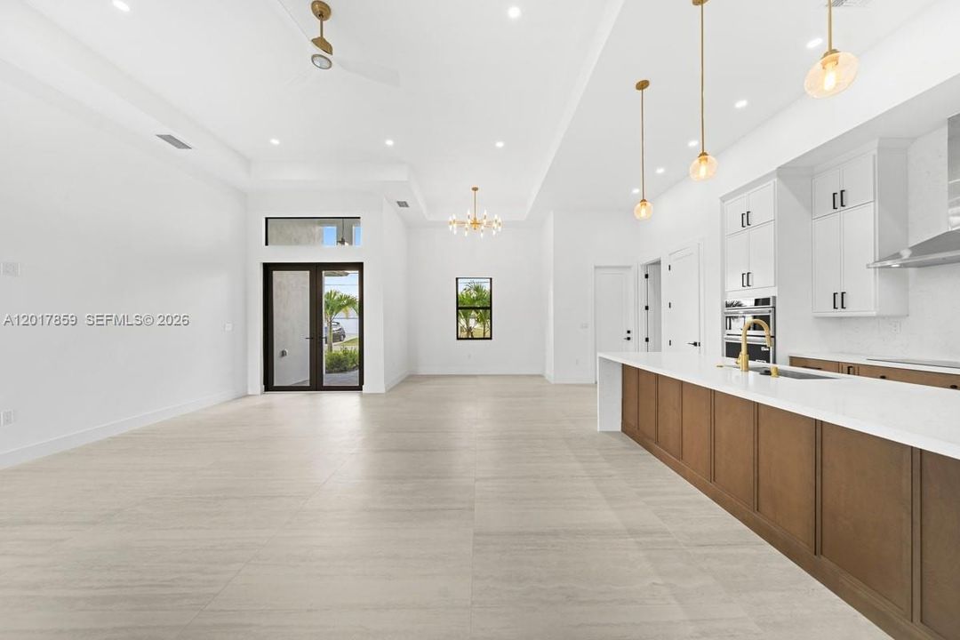 Open-concept interior featuring high ceilings with recessed lighting, large format floor tile, white shaker-style cabinetry, quartz countertops, and three gold-toned pendant lights over a spacious kitchen island