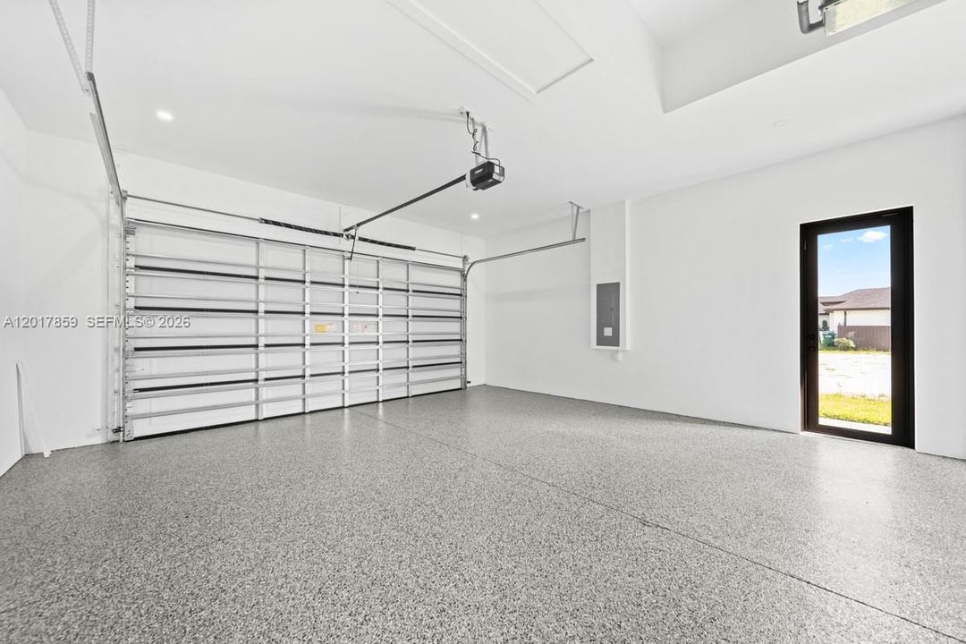 Finished garage featuring epoxy flooring, crisp white walls, recessed lighting, and a glass-paneled pedestrian door