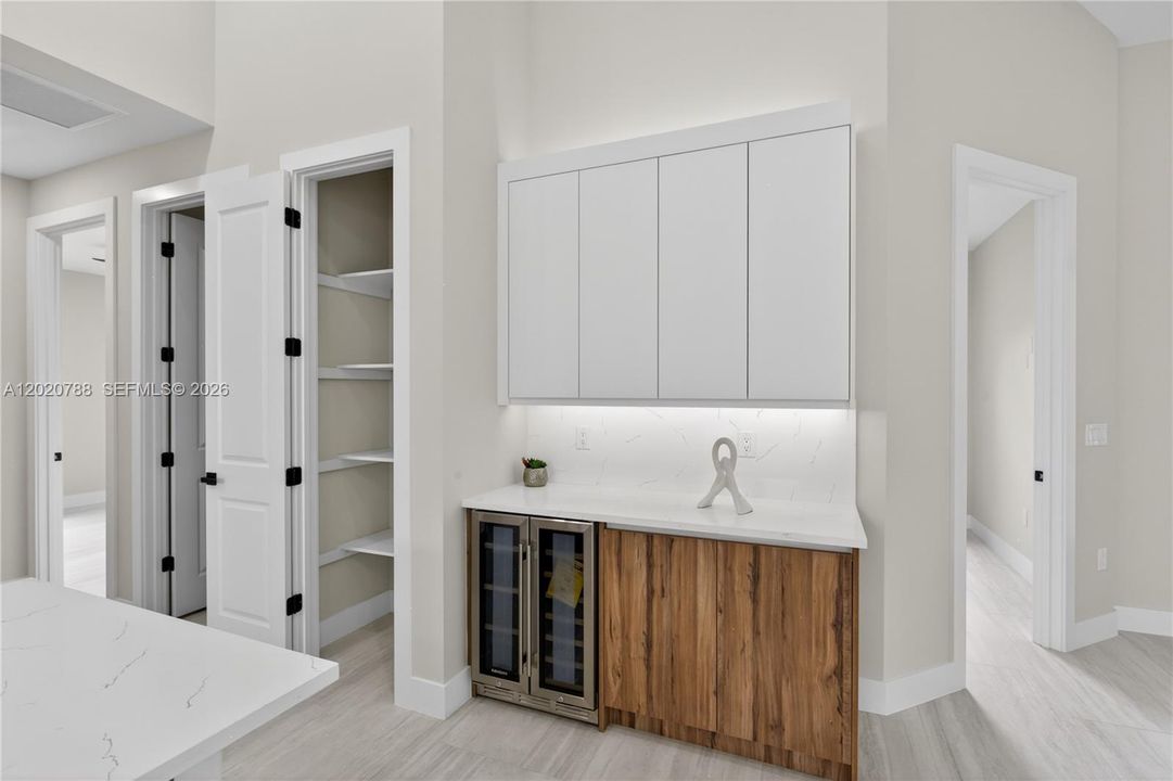 Built-in BUTLER’S PANTRY w/ warm WOOD-GRAIN cabinetry, sleek WHITE upper cabinets, QUARTZ countertops, under-cabinet lighting & built-in WINE REFRIGERATOR, ideal for BEVERAGE STATION, COFFEE BAR, or EXTRA STORAGE & PREP SPACE.