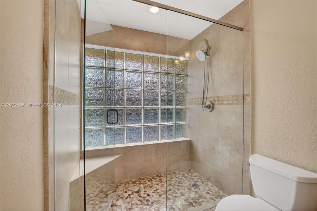 Primary bathroom w/ upgraded tile, double vanity with granite counter, and oversized shower w/ bench & glass door enclosure