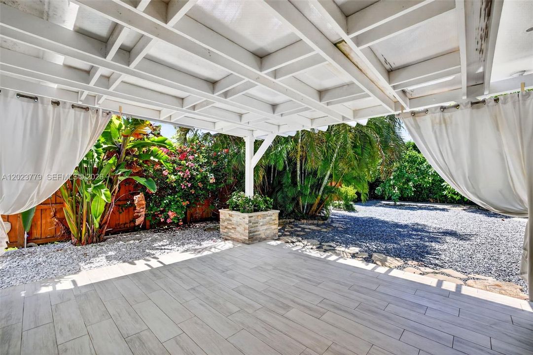 Covered patio overlooking backyard, tiled floor and stacked stone planter