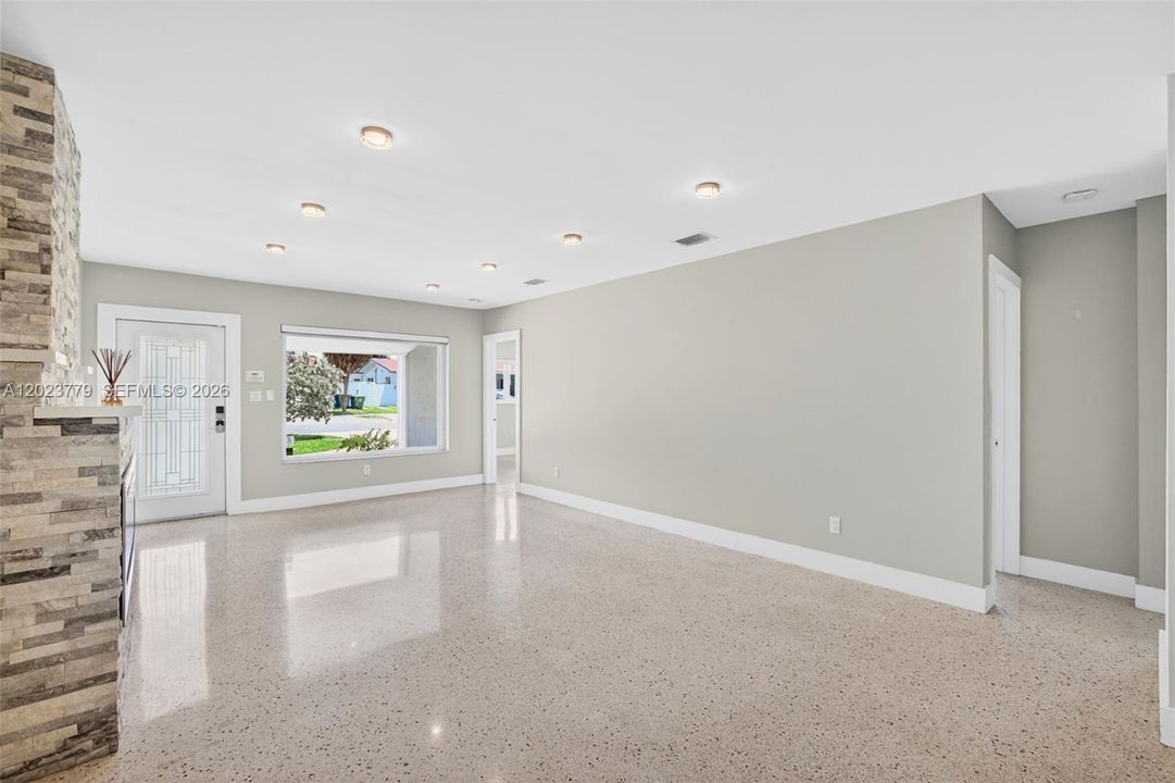 Stacked Stone Electric Fireplace with color changing light, lots of high hat lighting, beautiful restored polished terrazzo flooring. Flat ceilings and neutral beautiful paint, large impact window overlooking front yard. Hallway on right leads to two guest bedrooms