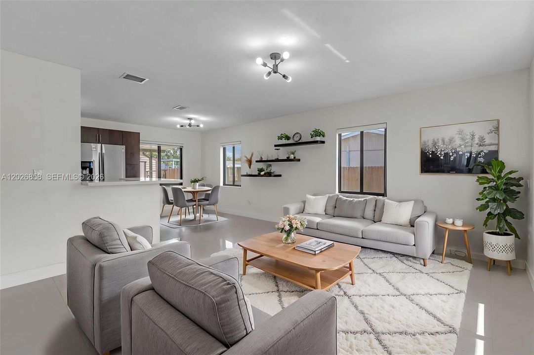 Open and airy living room with modern finishes, oversized tile flooring, custom accent wall, and seamless flow into the kitchen and dining area.