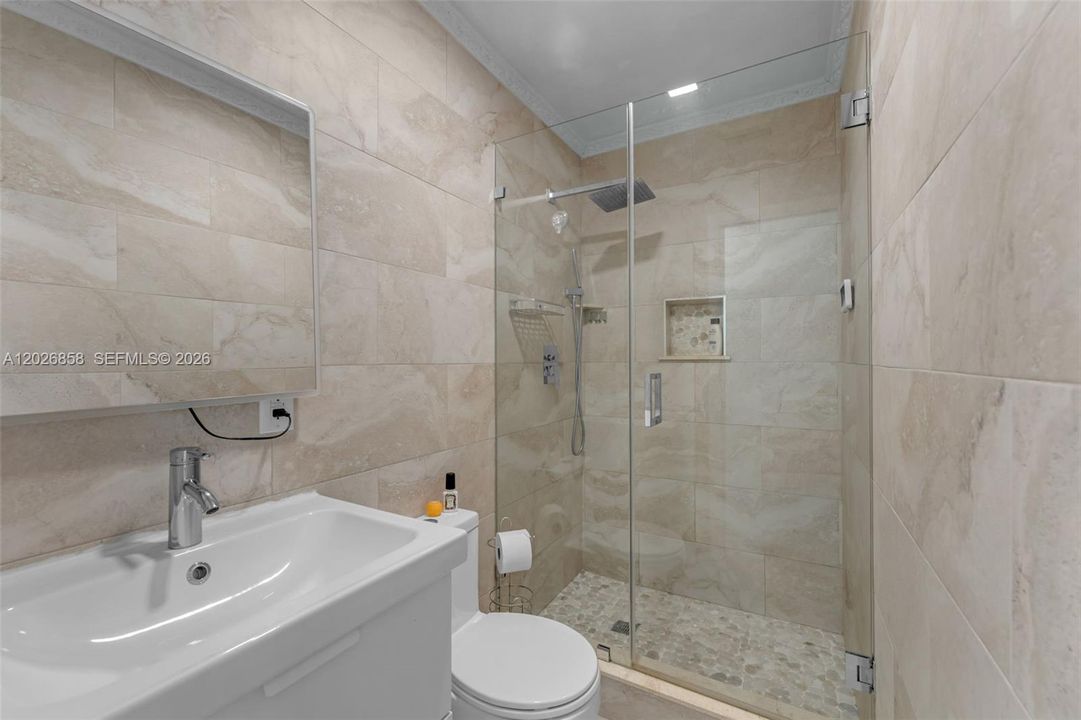 Tastefully remodeled guest bathroom with floor-to-ceiling tile and frameless glass shower enclosure.