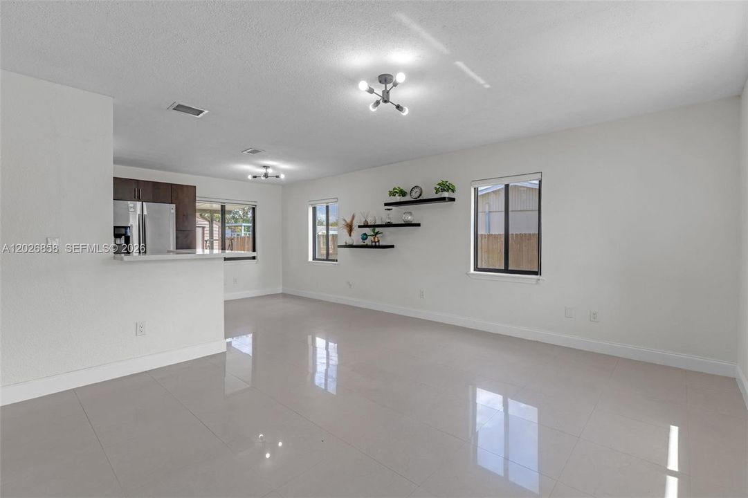 Open and airy living room with modern finishes, oversized tile flooring, custom accent wall, and seamless flow into the kitchen and dining area.