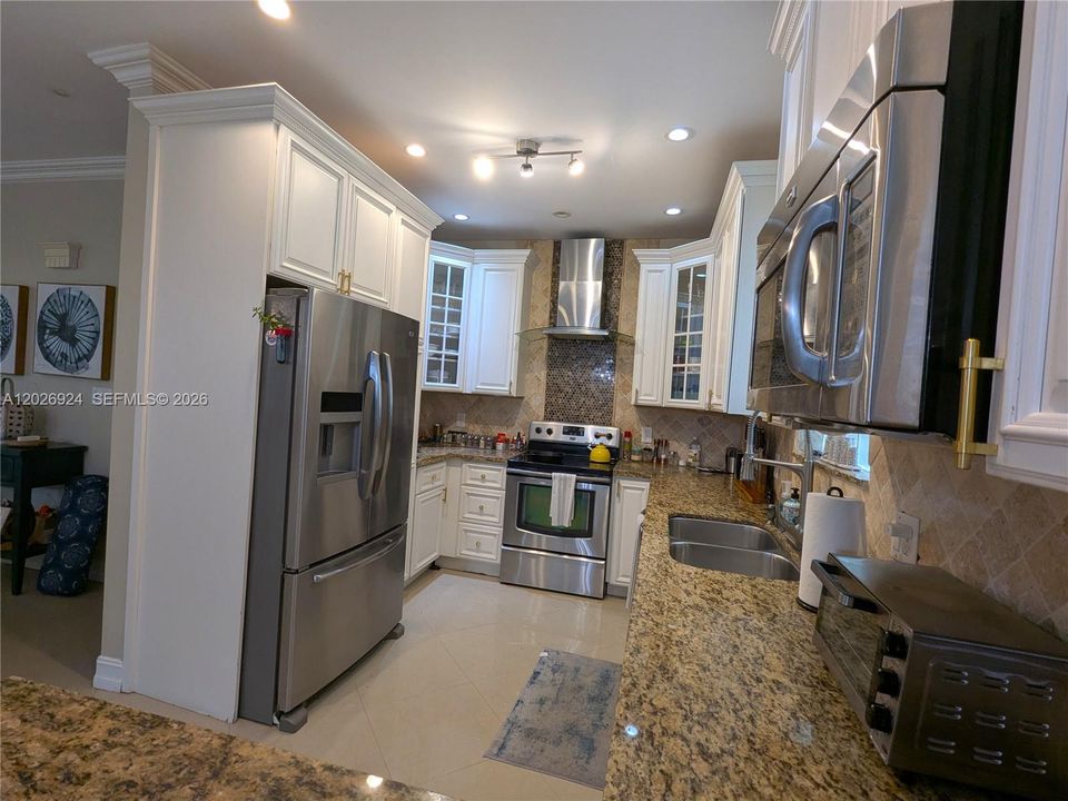 Spacious kitchen with stainless-steel appliances, granite countertops, white cabinetry, accent backsplash, modern hood, and a well-organized layout that highlights both workspace and storage.