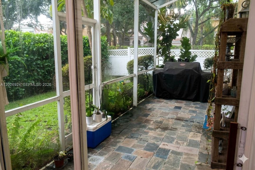 Lush landscape view from the screened-in patio. Stone tile flooring, and room for a covered grill area, offering a comfortable outdoor space protected from the elements.