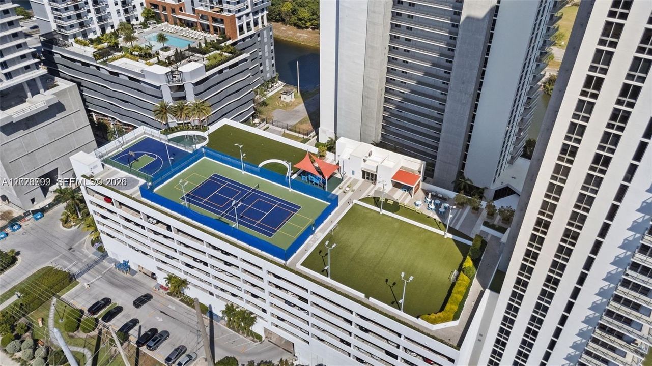 Elevated amenity level featuring tennis courts, open green spaces, and shaded lounge areas for entertainment and recreation.