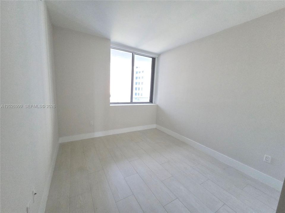 Well-proportioned bedroom with a large window offering natural light and partial skyline views. Clean finishes and neutral tones create a flexible, modern space.