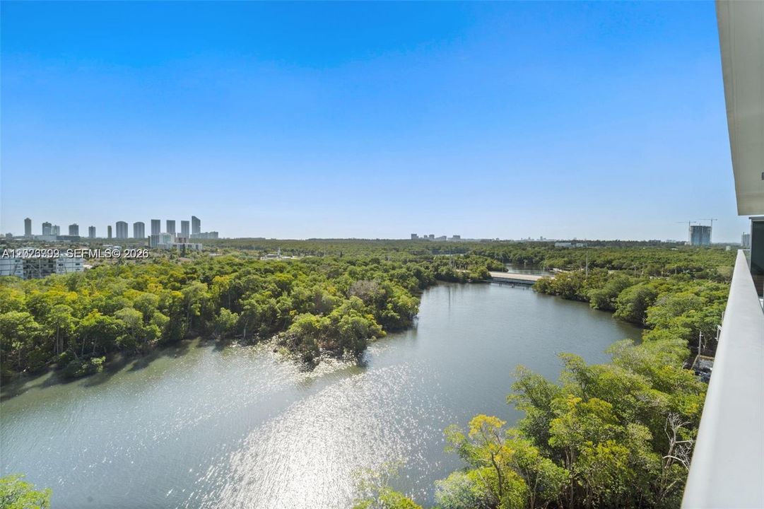 Wide water views stretch over the surrounding greenery, with skyline views visible in the distance. The elevated perspective highlights the property’s scenic waterfront setting.