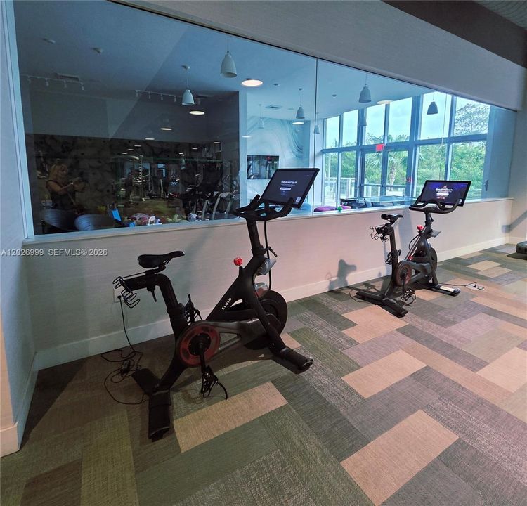 Stay active in the modern fitness studio, featuring high-end Peloton stationary bikes with a view of the facility's extensive amenities.