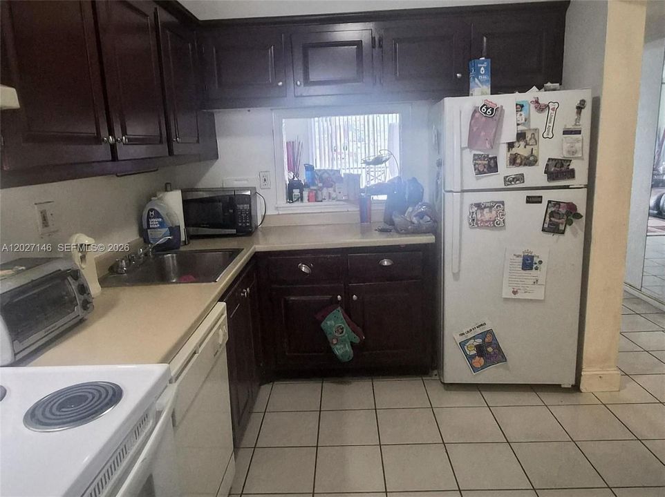 Efficient galley kitchen with cabinetry, ample counter space for meal prep, matching appliances, washer/dryer, clean tile flooring, and a bright central lighting strip.
