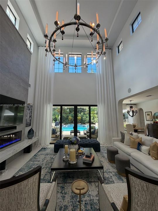 GREAT ROOM HAS FLOOR TO CEILING CUSTOM MADE WINDOW TREATMENTS AND A BEAUTIFUL TILED WALL WITH A FLOATING MARBLE MANTEL SHOWCASING AN ELECTRIC FIREPLACE.  VIEWS OF THE RESORT STYLE POOL/SPA AREA.