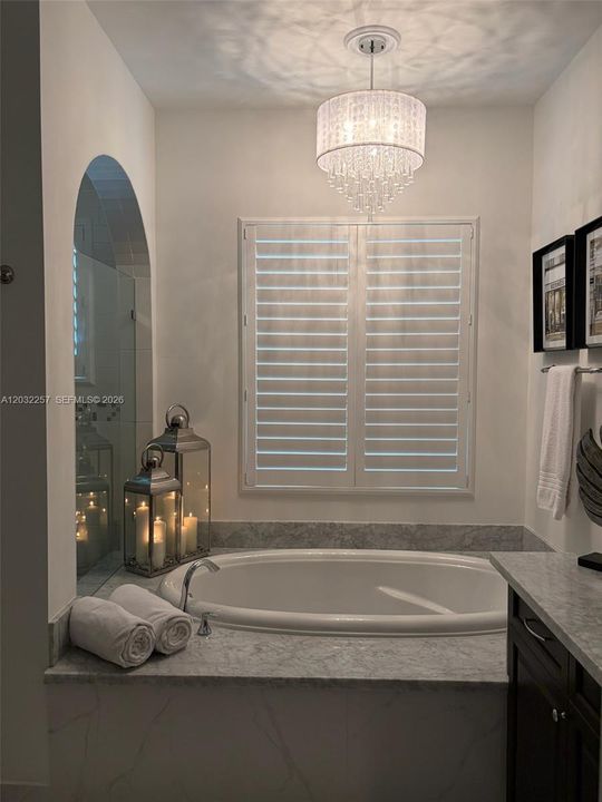 GARDEN TUB SURROUNDED BY MARBLE, AND CEILING DECORATED WITH A BEAUTIFUL CRYSTAL CHANDELIER.