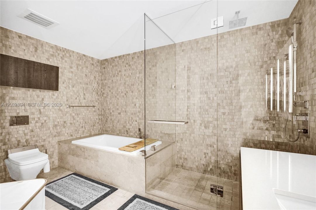 Primary bath with dual vanity, illuminated mirrors, glass shower and stone finishes.