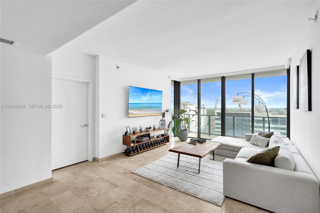 Open living room with floor-to-ceiling glass, city views and balcony access.