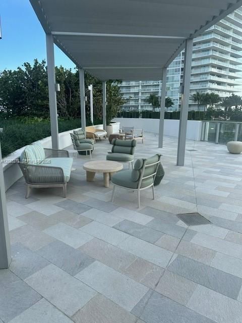 Outdoor terrace featuring light-toned stone tile flooring, a metal pergola, low-profile perimeter walls, and built-in wall-mounted lighting