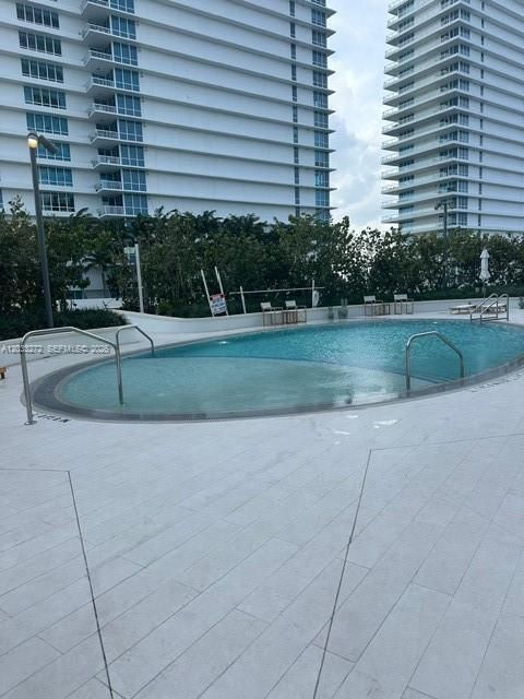 Oval swimming pool with metal handrails and a light-toned stone-finish pool deck