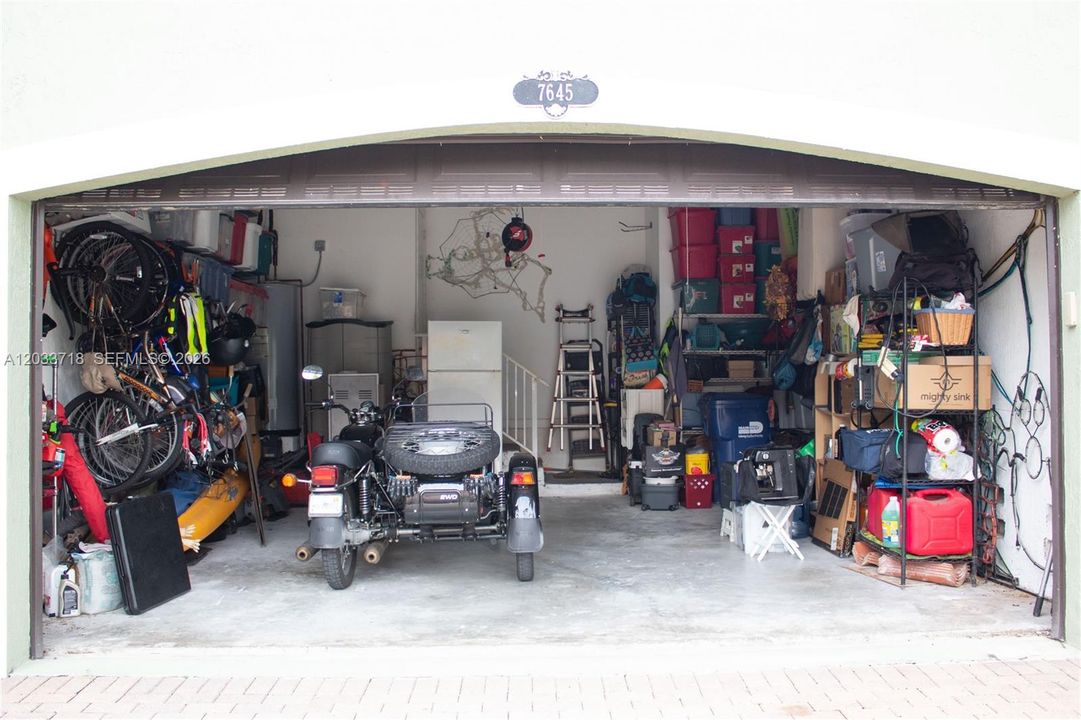 Garage has an independent Electronic Vehicle (EV) Charging Outlet on the right wall. There are steps that lead to the interior of the home in the middle of the photo.