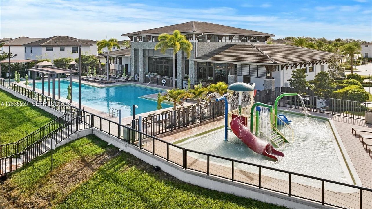 Impressive aerial view of the resort-style amenity complex, featuring a sprawling lap pool alongside a vibrant interactive splash pad. Lush palm-lined grounds and a grand clubhouse complete this exceptional community retreat.