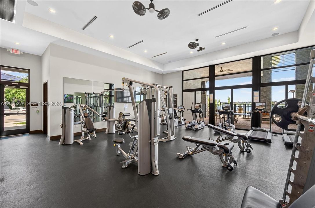 State-of-the-art fitness center equipped with premium strength and cardio machines for a complete workout. Floor-to-ceiling windows flood the space with natural light and offer scenic views of the outdoor terrace beyond.