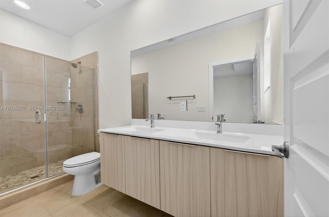 Spa-like primary bath featuring a sleek frameless glass shower with pebble-stone flooring and a floating double-sink vanity. A full wall mirror amplifies the bright, light-filled space throughout.