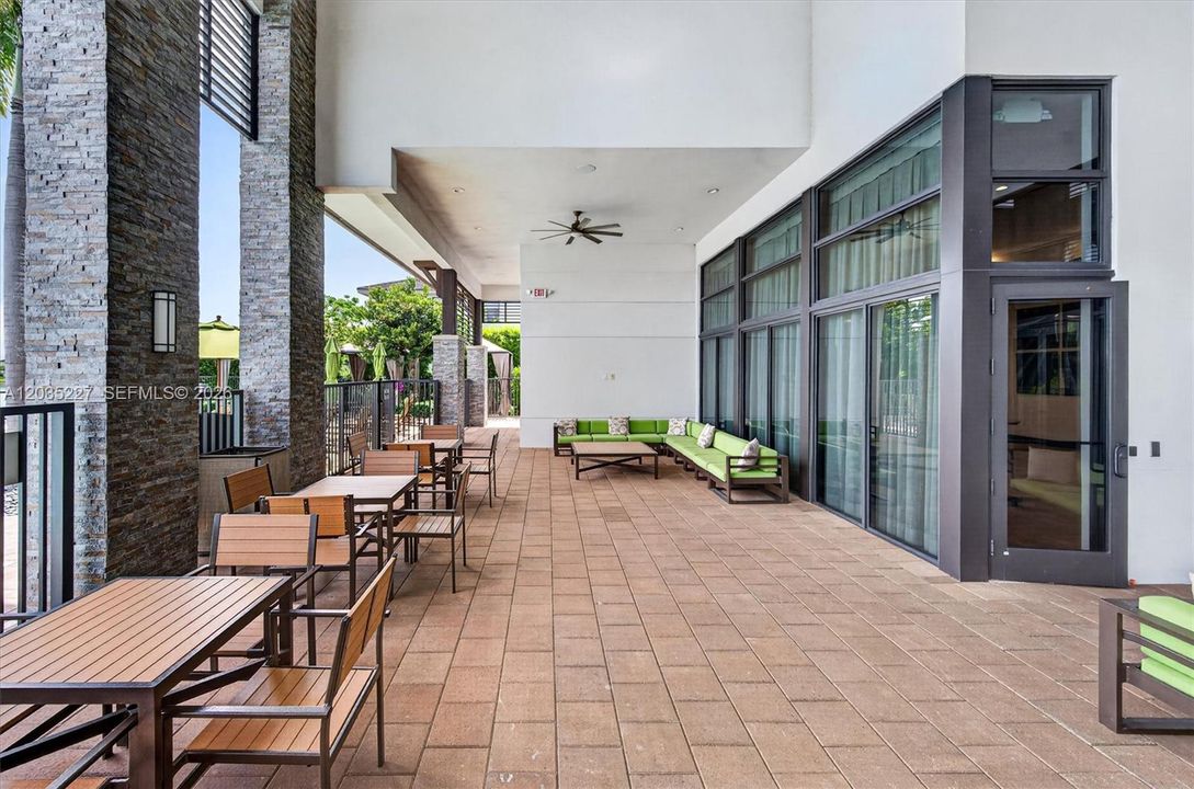 Resort-style covered terrace offering plenty of shaded seating for residents to relax or socialize. Stacked-stone columns, ceiling fans, and vibrant green lounge furniture create a sophisticated outdoor entertainment area.
