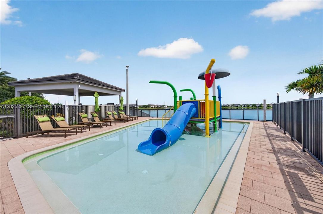 Impressive aerial view of the resort-style amenity complex, featuring a sprawling lap pool alongside a vibrant interactive splash pad. Lush palm-lined grounds and a grand clubhouse complete this exceptional community retreat.