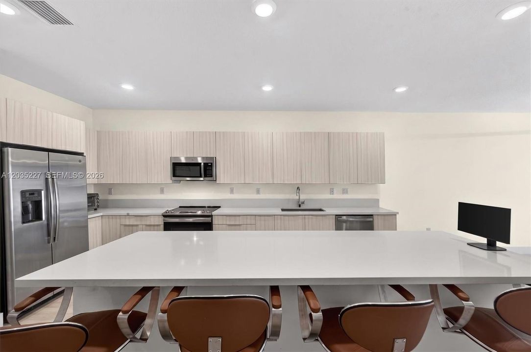 Expansive eat-in kitchen with a generous quartz island and stylish leather counter stools. Full stainless steel appliance suite includes a French-door refrigerator, while sleek wood-grain cabinetry offers abundant storage.