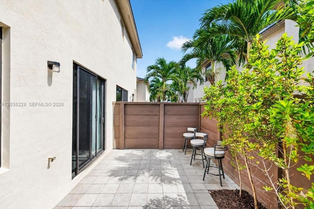 Private paver patio offering an inviting outdoor retreat, framed by a wood privacy fence and tropical landscaping. Sliding glass doors provide seamless indoor-outdoor flow, perfect for South Florida living.