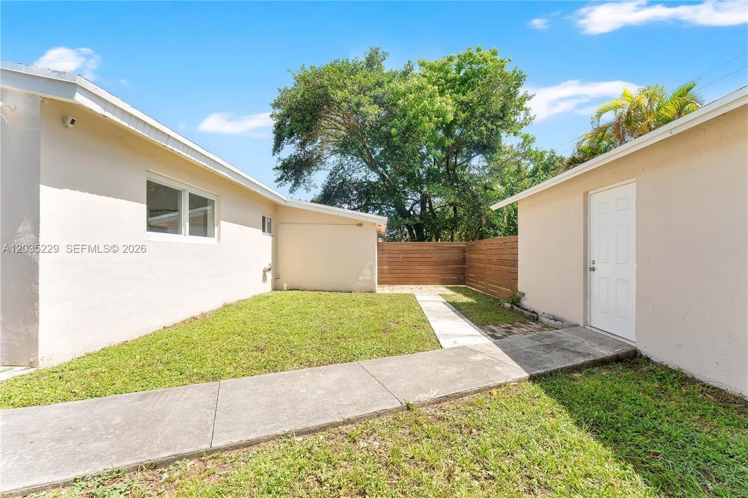Private backyard with lush green lawn, mature shade trees, horizontal wood privacy fence, and a separate entrance to the guest/in-law unit.